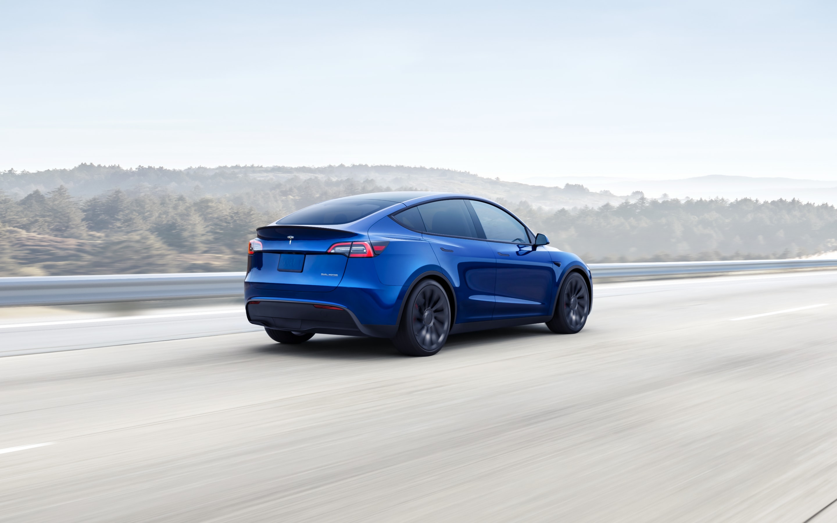 Metallic blue Model Y driving down a hillside highway